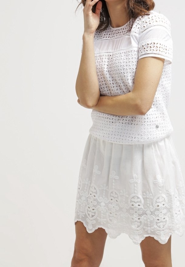 Weißes Kleid mit einem strukturierten Häkel-Oberteil und einem durchsichtigen, bestickten Rock, der florale Muster und einen gewellten Saum aufweist. Kurze Ärmel.