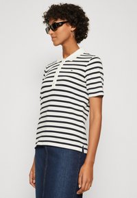 Polo a righe bianco e blu navy, con colletto, maniche corte e un piccolo logo sul petto; abbinato a una gonna di denim.