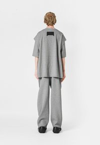 Camiseta gris de gran tamaño y pantalones de pierna ancha a juego, hechos de una tela suave. Presenta un acento de rectángulo negro en la parte posterior de la camiseta.