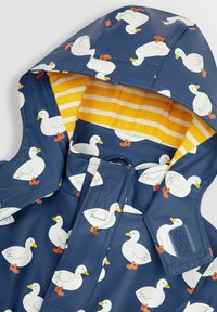 Imperméable bleu en caoutchouc avec des motifs de canard. Doublure à rayures jaunes à l'intérieur de la capuche et fermetures Velcro. Matériau imperméable avec une texture lisse.