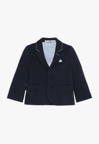 Granatowa marynarka na dwa guziki, z wyłogami z wycięciem, przednimi kieszeniami oraz jasnoniebieską podszewką w kropki. Na klapach znajdują się białe przeszycia jako akcenty.