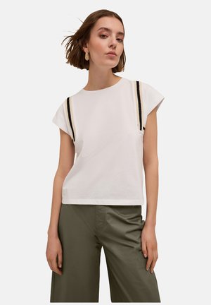 White cotton T-shirt with short sleeves, featuring black and cream stripes along the shoulders. Paired with olive green wide-leg trousers.
