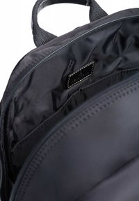 Lo zaino in tessuto nero presenta un compartimento principale, una fodera liscia e una piccola etichetta. Chiusura con zip e manici in tessuto resistenti sono ben visibili.