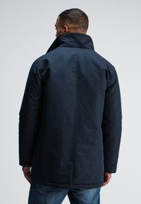 Marinewaterdichte jas met hoge kraag, gladde textuur, lange mouwen en een rechte snit, gecombineerd met blauwe jeans.