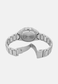 Orologio in acciaio inossidabile argentato con cassa rotonda, bracciale a maglie metalliche e chiusura. Presenta bordi ottagonali e una superficie liscia e lucida.