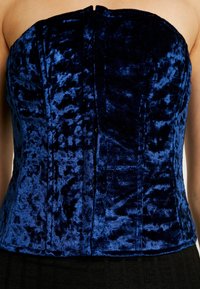 Top corpetto senza spalline in velluto blu intenso con superficie texturizzata, caratterizzato da cuciture verticali e una chiusura centrale. Design liscio e aderente.