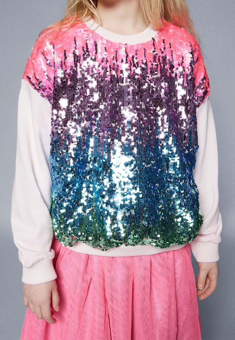 Sweatshirt orné de sequins avec un dégradé du rose au violet, passant au vert et au bleu. Manches douces et ourlet côtelé. Jupe rose en dessous.