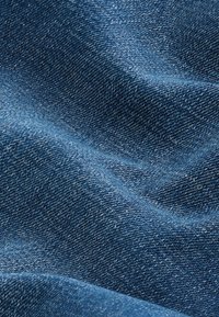 Gros plan sur un tissu en denim bleu texturé avec un motif de tissage visible et des plis doux créant des ombres et des reflets.