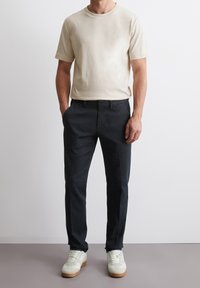 T-shirt beige in cotone con maniche corte, abbinata a pantaloni scuri. Scarpe da ginnastica bianche completano il look. Design semplice e moderno.