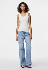 Vit ribbad linne med rundad hals, kombinerad med ljusblå vida jeans. Tyget verkar mjukt och något texturerat.