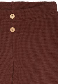 Tessuto a coste marrone con una texture morbida, caratterizzato da due bottoni in legno in vita e un design a vestibilità rilassata.