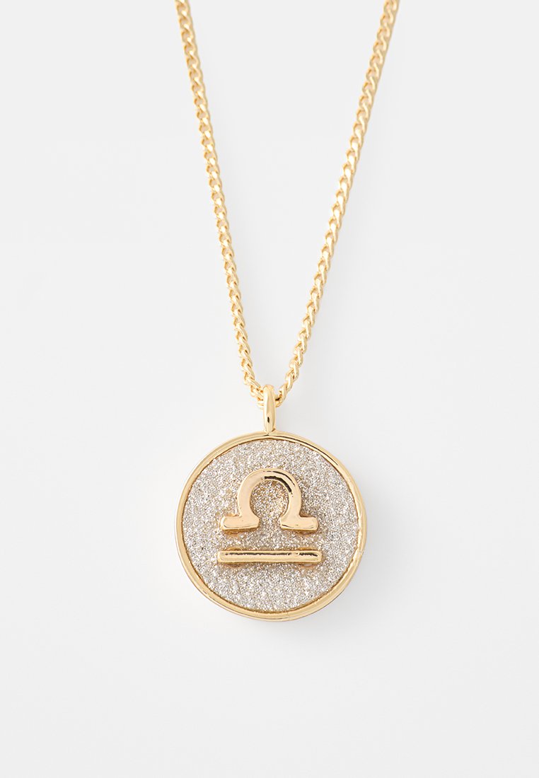 Goldene Halskette mit einem runden Anhänger, der einen silbernen Glitzerhintergrund und ein erhabenes Waage-Symbol in Gold aufweist. Die Kette hat ein gedrehtes Design.