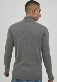 Maglione grigio a maglia con colletto alto, maniche lunghe e orlo a costine. La texture è liscia e aderente al corpo.