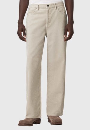 Beige kordfløjlsbukser med lige ben, båret med brune ruskindsstøvler og en hvid top, vist fra taljen til fødderne.