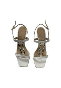 Sandali alti bianchi con tacco, punta quadrata, cinturini trasparenti e dettagli in hardware dorato con un elemento decorativo in cristallo.