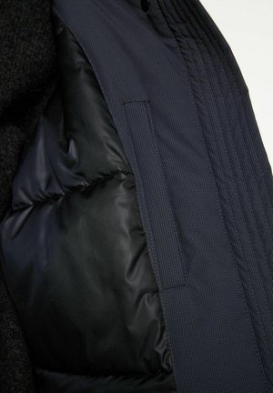 Padded jacket interior in dark navy with a smooth texture, featuring a pocket and vertical stitching details along the lining.