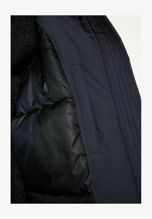 Padded jacket interior in dark navy with a smooth texture, featuring a pocket and vertical stitching details along the lining.