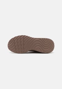 Rubber shoe sole in a light brown hue, featuring a wavy texture and horizontal grooves for traction. Flat, rounded toe design.