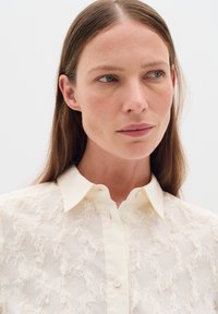 Cream-colored shirt with a textured, frayed pattern. Features a classic collar and hidden button placket. Soft, lightweight fabric.