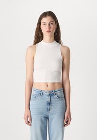 Valge ribiline lühike top kõrge kaelusega ja ilma varrukateta, millele on lisatud helesinised kõrge vöökohaga teksad. Sile tekstuur, minimalistlik stiil.