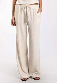 Pantalones anchos beige con cintura ajustable, fabricados con un tejido ligero y texturizado. Incluyen bolsillos laterales y un ajuste relajado.