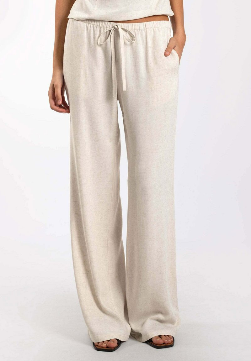 Pantalons beige à jambe large avec taille à cordon de serrage, fabriqués à partir d'un tissu léger et texturé. Comprend des poches latérales et une coupe décontractée.
