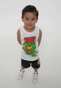 Canotta bianca con una grafica di un personaggio tartaruga verde e la parola "RAPH" in rosso. Pantaloni corti neri con accenti colorati. Sneakers bianche.