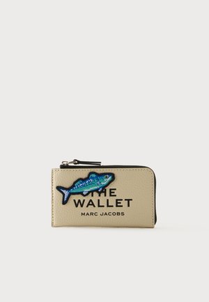 Portefeuille beige Marc Jacobs avec fermeture éclair noire, écusson poisson bleu brodé et texte en gras THE WALLET et MARC JACOBS sur le devant.