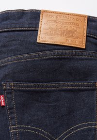 Mörkblå denimjeans med en läderlapp, med orange sömmar och en röd Levi's tag. Etiketten visar storlek W32 L32, stil Lot 502.