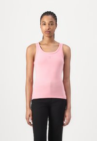 Débardeur rose sans manches avec un décolleté rond. Présente un logo discret sur la poitrine. Le matériau est lisse et ajusté, associé à un pantalon noir.