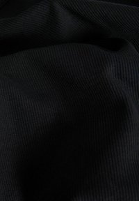 Svart ribbet stoff som viser en glatt tekstur med hevede linjer. Materialet ser mykt ut og faller lett, noe som fremhever elastisiteten.