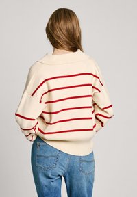 Maglione crema con strisce orizzontali rosse, vestibilità oversize, colletto a coste e maniche con polsini, abbinato a jeans di denim blu chiaro.