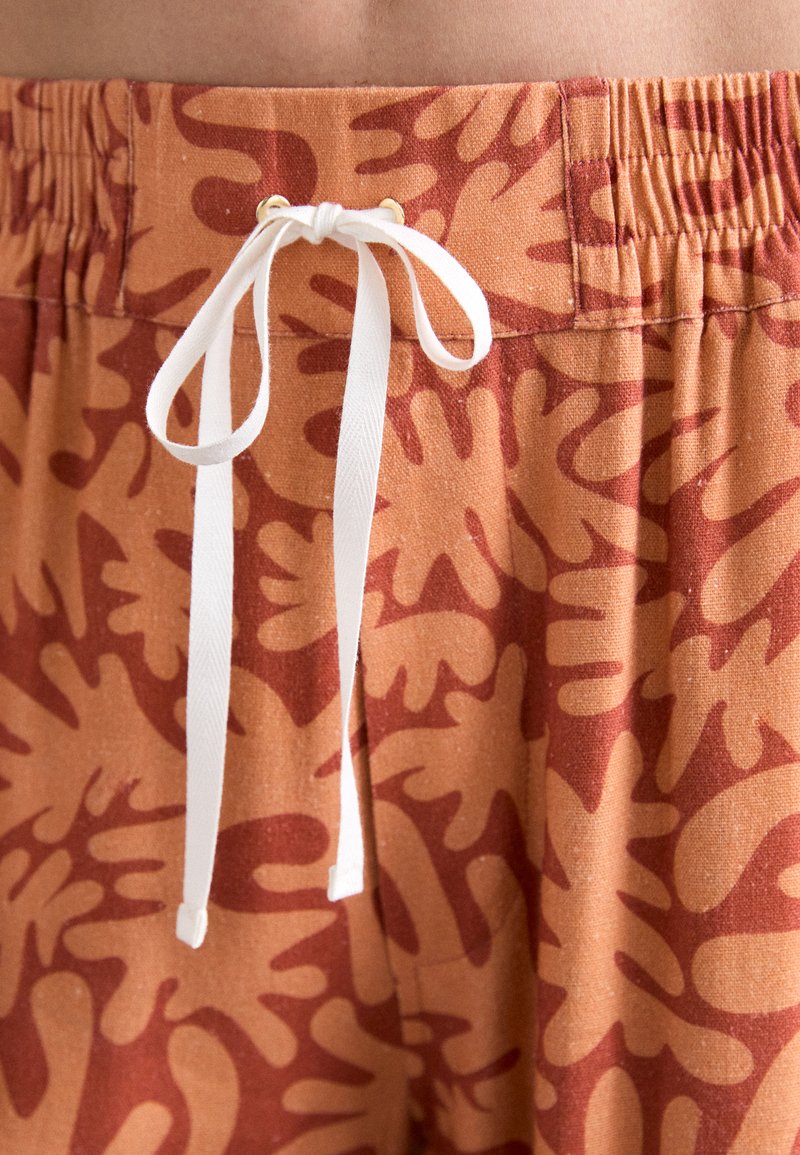 Brown cotton shorts featuring a coral abstract pattern, elastic waistband with a white drawstring, and gold-tone eyelets.