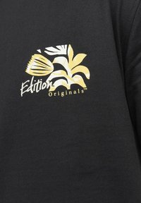 Čierne bavlnené tričko s žltou grafickou potlačou listov a kvetu s textom "Edition Originals" v štýlovom písmovom type.