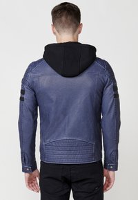 Chaqueta de motocicleta azul marino con capucha negra, que presenta detalles acanalados en los hombros y un acabado texturizado. Diseño ajustado con puños de presión.