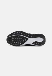 Sole di scarpa atletica nera con un design in gomma testurizzata, caratterizzata da motivi esagonali e un accento bianco sul tallone.