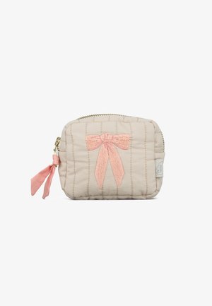 Petite pochette matelassée beige avec un nœud brodé rose sur le devant et une languette de fermeture éclair en tissu rose sur le côté gauche.