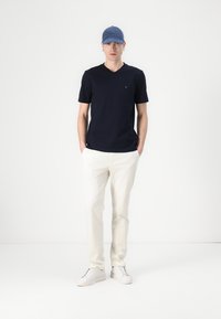 Mornarsko plavi T-shirt s V izrezom uparen s bijelim hlačama i bijelim tenisicama. Svijetloplavi šešir upotpunjuje odjevnu kombinaciju. Minimalistički dizajn i pamučna tkanina.
