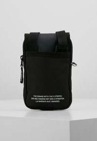 Borsa nera in tessuto con chiusura a zip, due manici superiori e logo frontale in bianco. Texture liscia e forma rettangolare compatta.