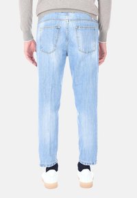 Jeans in denim azzurro chiaro con vestibilità relax, caratterizzati da cinque tasche e una leggera scoloritura. Abbinati a sneakers bianche e a un maglione grigio.