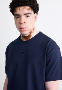 Tamsiai mėlyna Nike marškinėliai, pagaminti iš minkštos medžiagos, su mažu išsiuvinėtu logotipu krūtinėje ir klasikine apvalia iškirpte.
