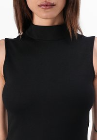 Black sleeveless top with a high neck, made of smooth, stretchy fabric. Features a fitted silhouette, emphasizing contour without embellishments.