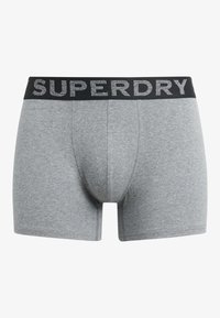 Boxer shorts en coton gris avec une taille noire portant l'inscription argentée "SUPERDRY". Texture lisse, design ajusté, longueur mi-cuisse.