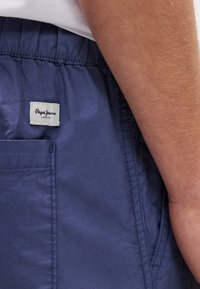 Σκούρο μπλε σορτς από ελαφρύ ύφασμα, με ελαστική μέση και μικρή λευκή ετικέτα με τη φράση "Pepe Jeans London" στην τσέπη.