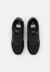 Black athletic shoes with a sleek design, featuring synthetic upper, wide textile straps, and padded collar for support. Size label visible.