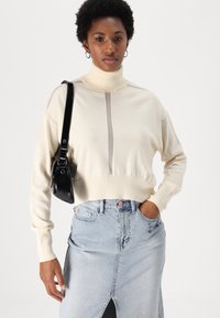 Kreto krēkļa svīteri ar ribotu apakšmalu un centrālo pelēko svītru, kombinējot ar gaišas džinsa svārki ar priekšējo šķēlumu un kabatām.