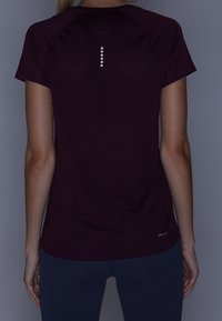 Bordowa sportowa koszulka z krótkim rękawem, z refleksyjnym pionowym akcentem z tyłu oraz etykietą "DRI-FIT" w pobliżu brzegu.