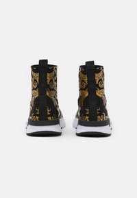 Svarta högklackade sneakers med gyllene ornamentmönster, utrustade med dragflik, vit mellansula och svarta yttersulor. Övre del i texturerat tyg.