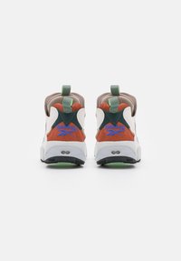 Baskets blanches et oranges avec des accents verts, un col rembourré, des surfaces texturées et des détails de logo. Présente une semelle extérieure noire.