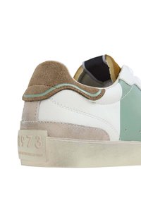 Zapatilla baja con cuero blanco, acentos en verde menta y una pestaña de talón de gamuza marrón. Suela texturizada con el número "1973" en relieve.